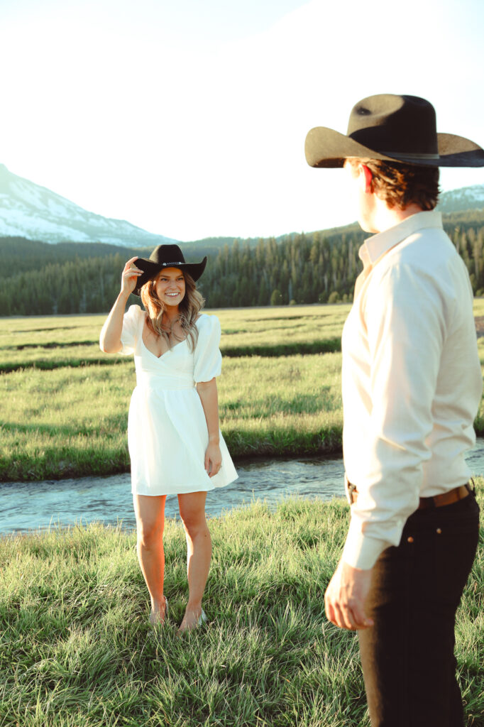 A girl standing with a cowboy hat on and a guy admiring her