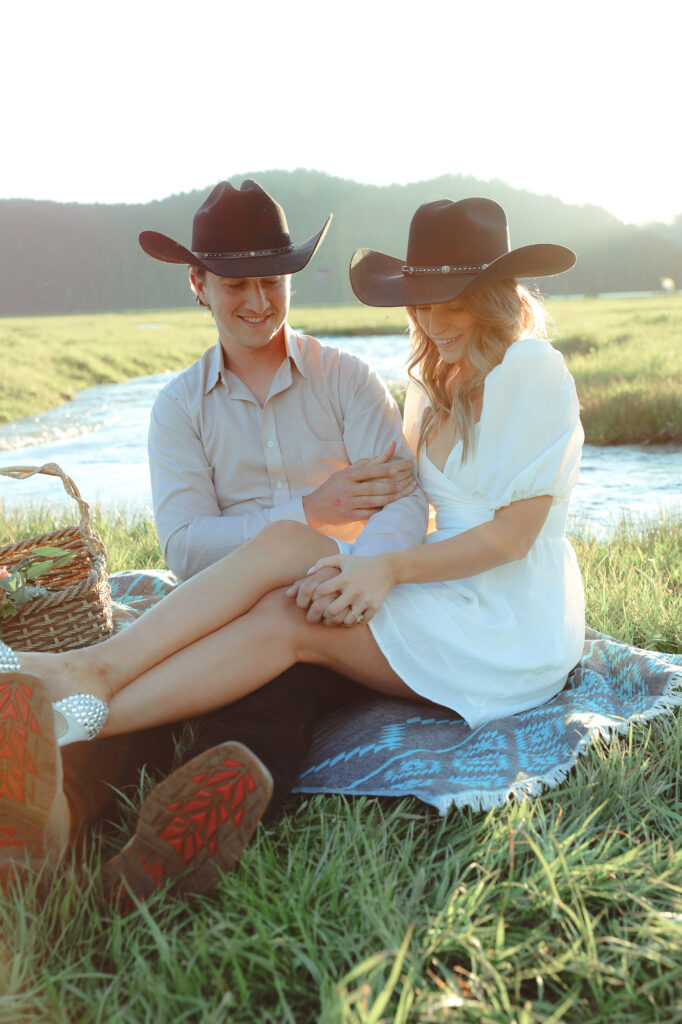 Couple sitting on a blanket with a basket of flowers with cowboy hats on