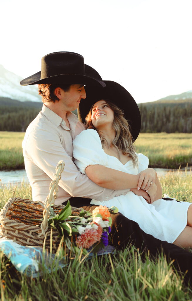 for their engagement photo shoot a couple sits on a blanket with a basket of flowers