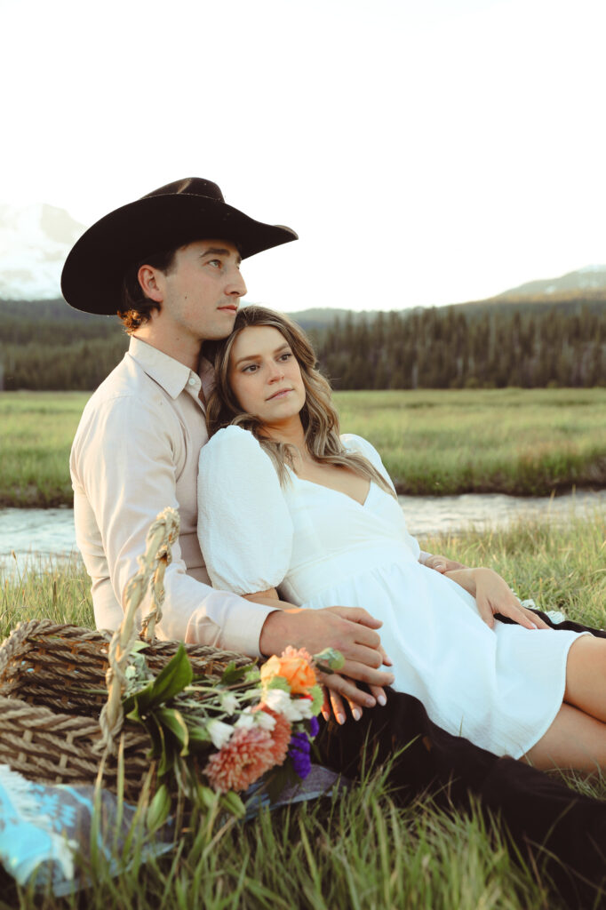 Couple sitting on a blanket with a basket of flowers posing for their engagement shoot