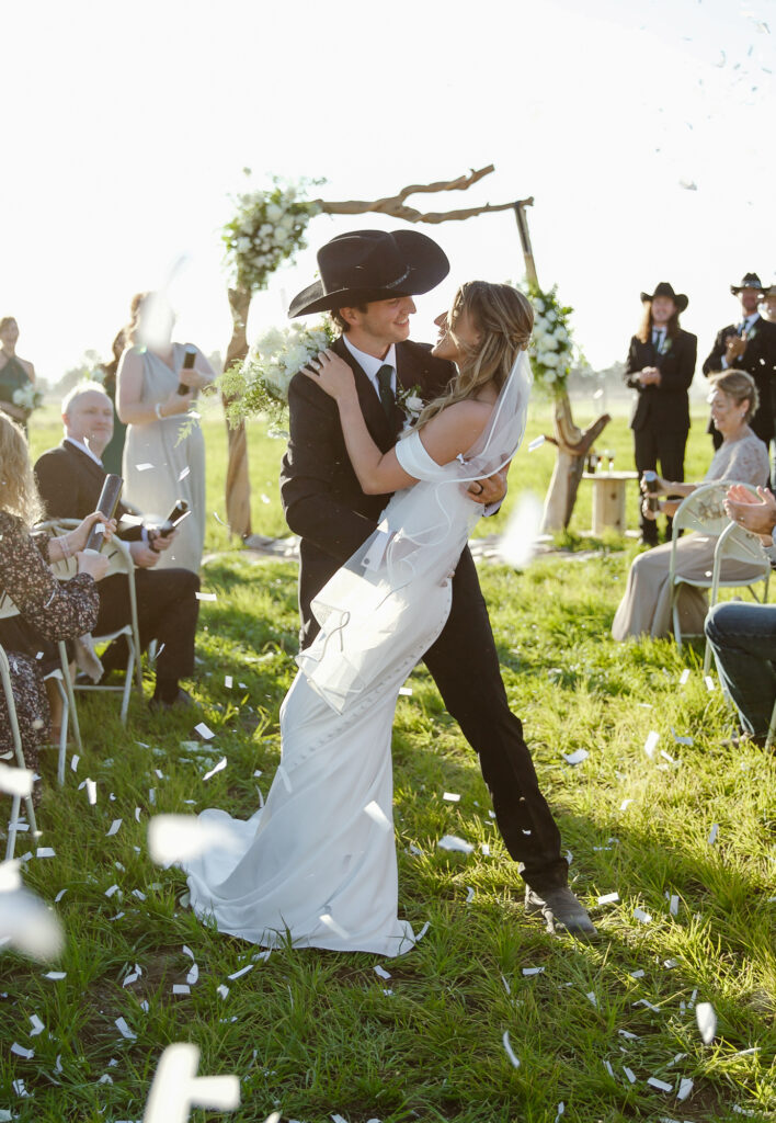 A couple about to dip with confetti surrounding them for their western wedding.