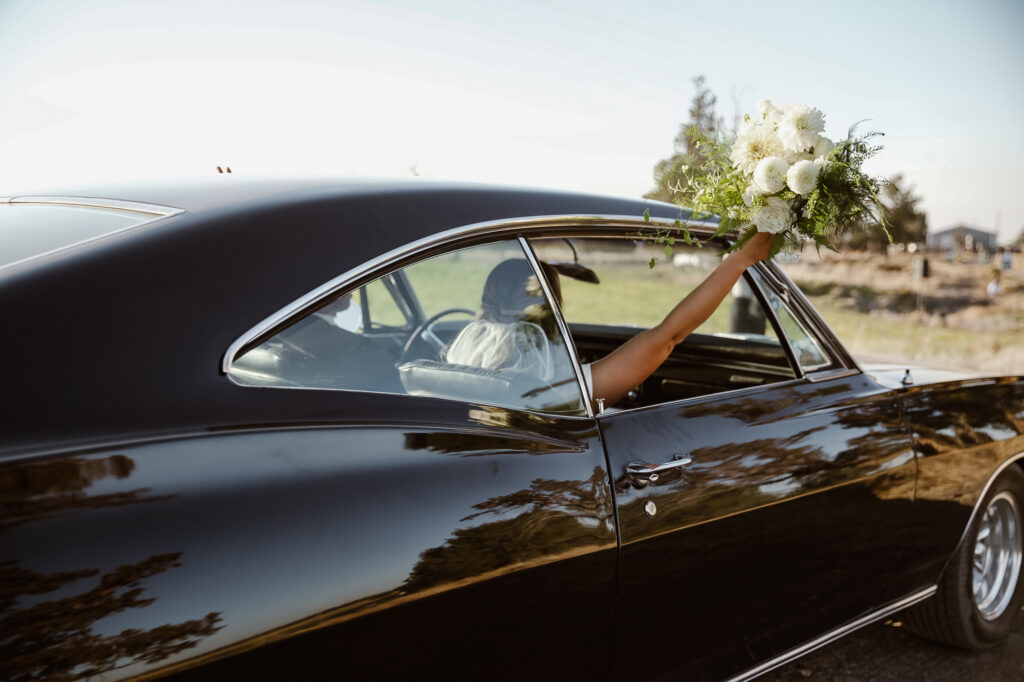 Bride holding bouquet out the window of their black car