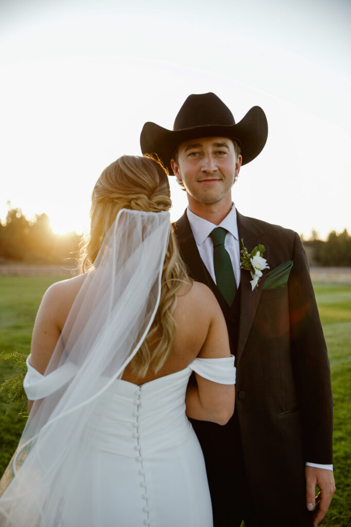 Couple posing. groom facing the camera, bride facing away at their western wedding.