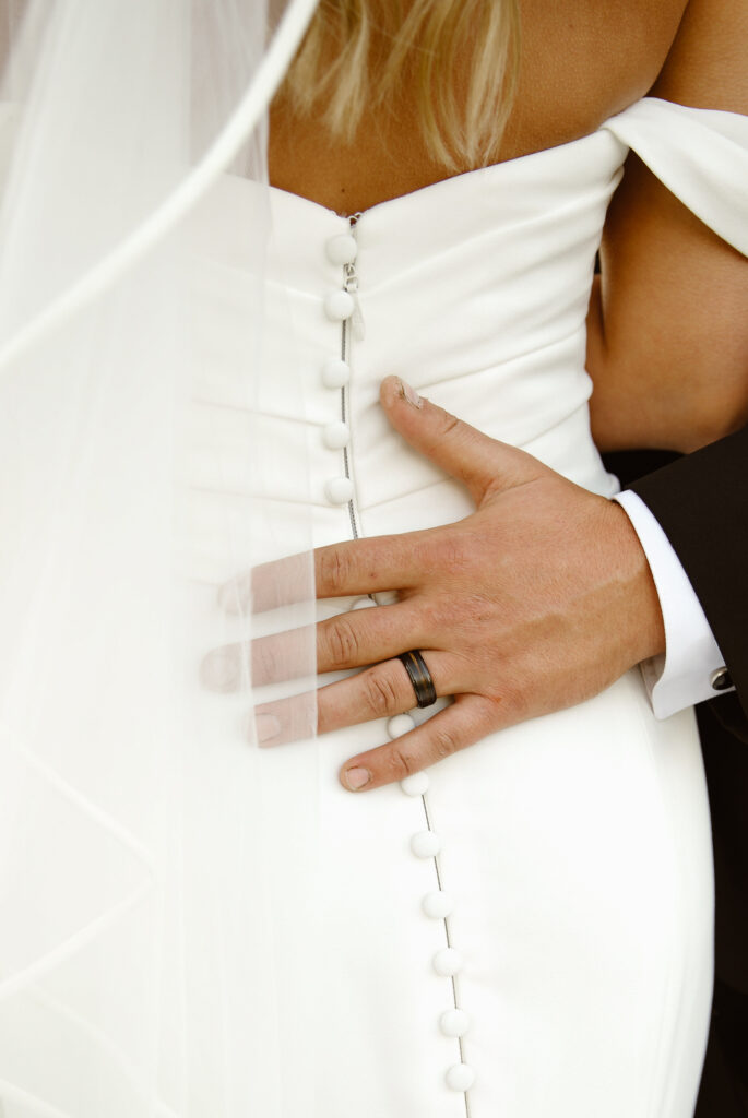 Grooms hand on Brides back showing off the buttons of her dress
